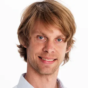 En man i vit skjorta som ler mot kameran.